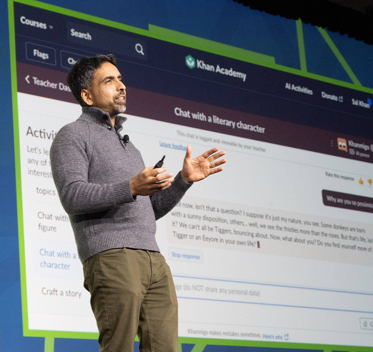 Khan Academy Founder Sal Khan stands on stage controlling a presentation screen while addressing 2023 AEC Second General Session audience