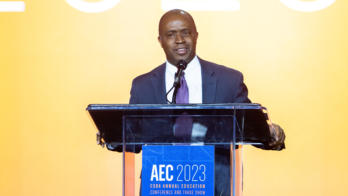 State Superintendent of Public Instruction Tony Thurmond dressed in a suit and tie stands at AEC 2023 podium