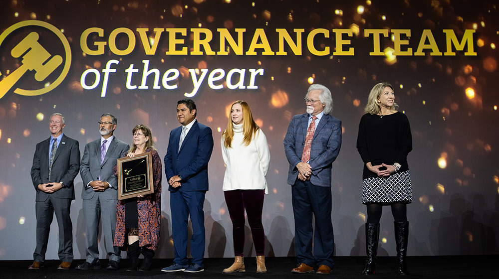 members of the Visalia USD Governance Team stand on a stage against a background screen that reads: Governance Team of the Year