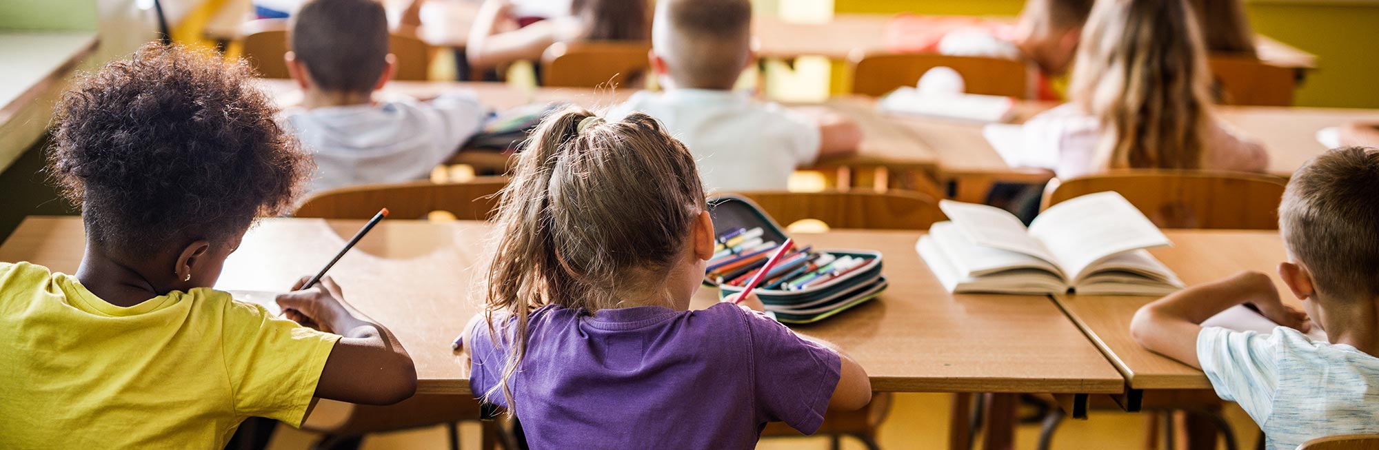 Young students sitting at desks working in a classroom, seen from behind