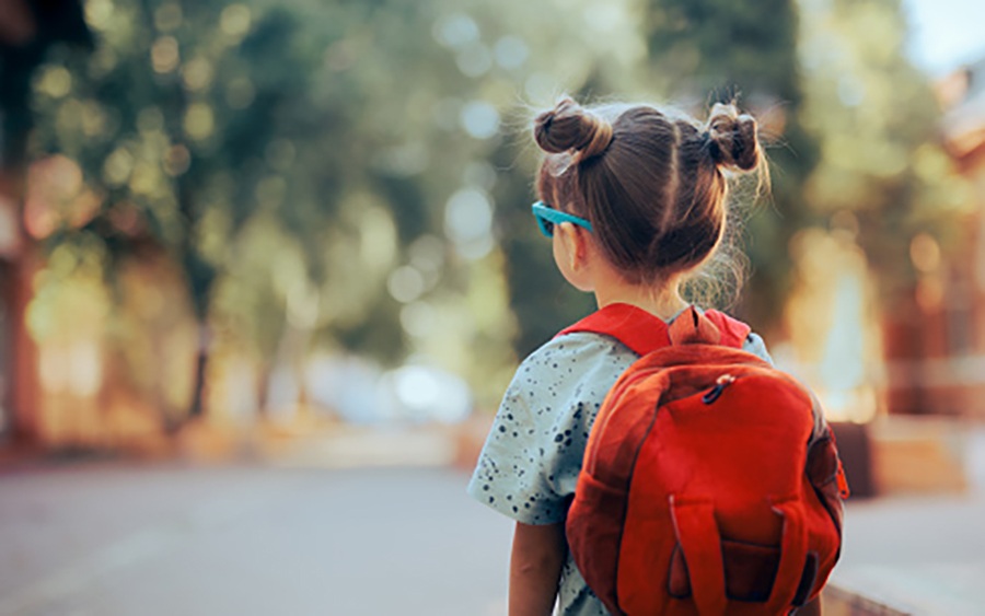 female child wearing a red backpack on her shoulders, blue sunglasses on her face, and two buns in her hair