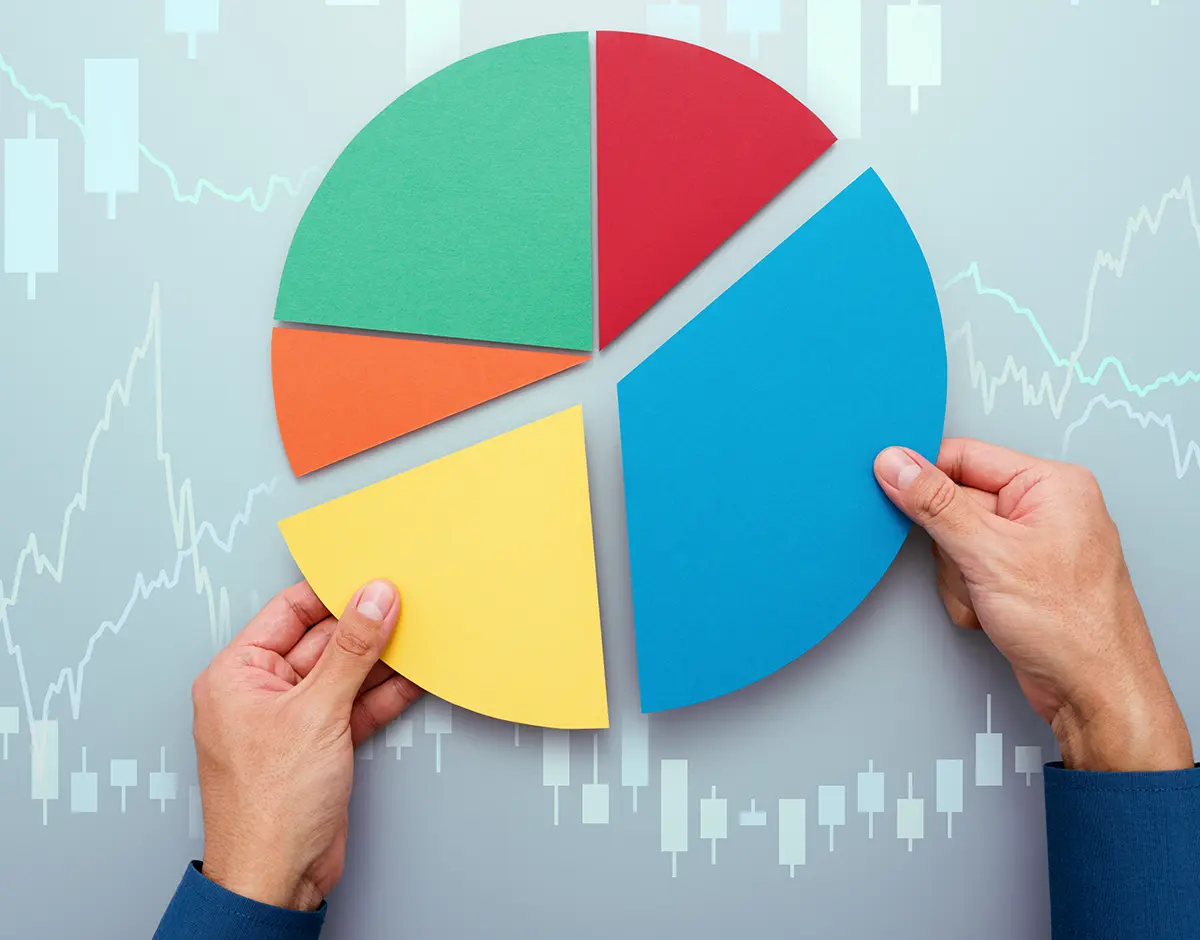 a colorful pie chart consisted of the colors green, red, blue, yellow, and orange; a hand each holds the larger yellow and blue wedges of the chart that sits on a background made of ascending and descending line graphs