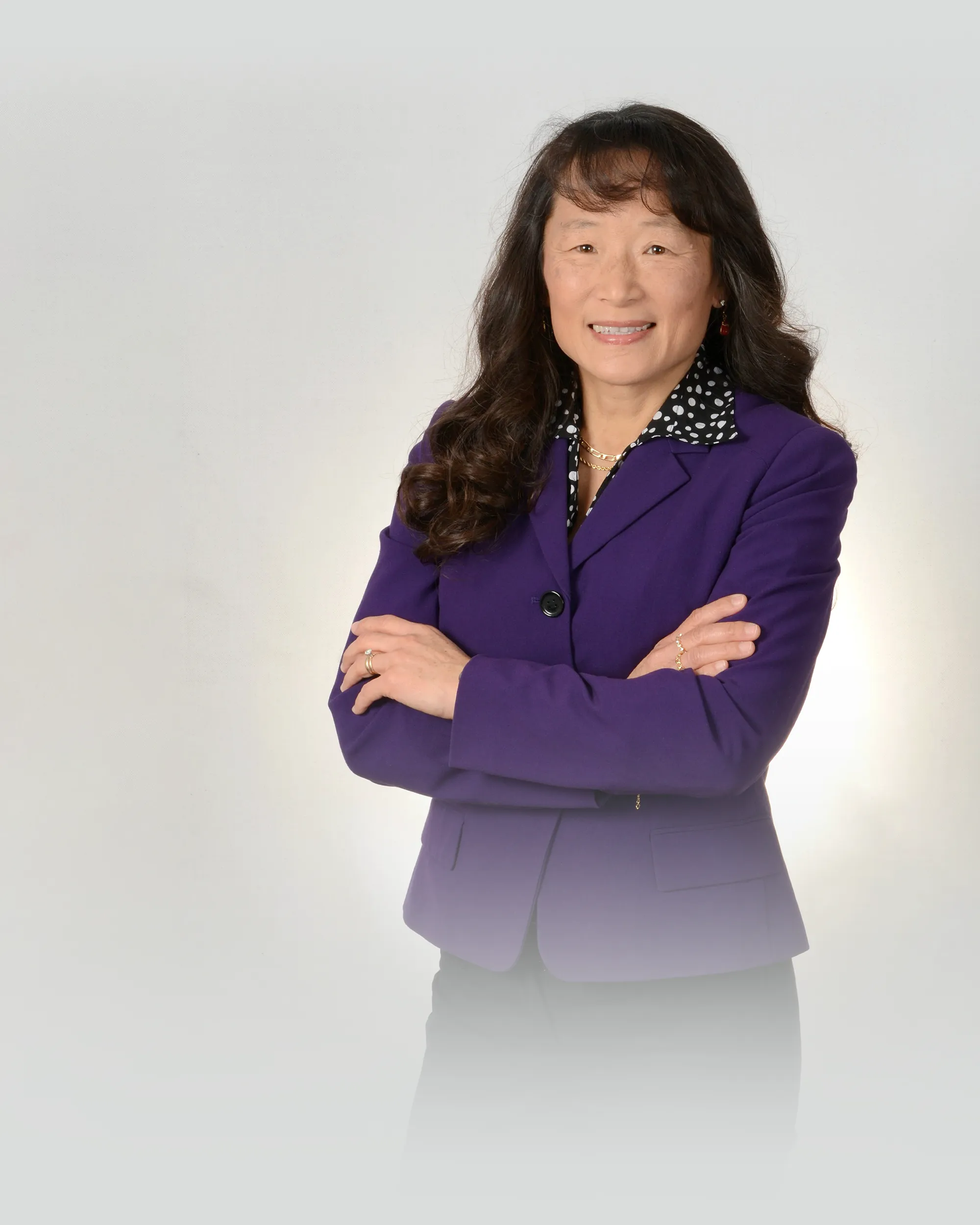 Kristie Wang wearing a purple blazer with her arms crossed and smiling