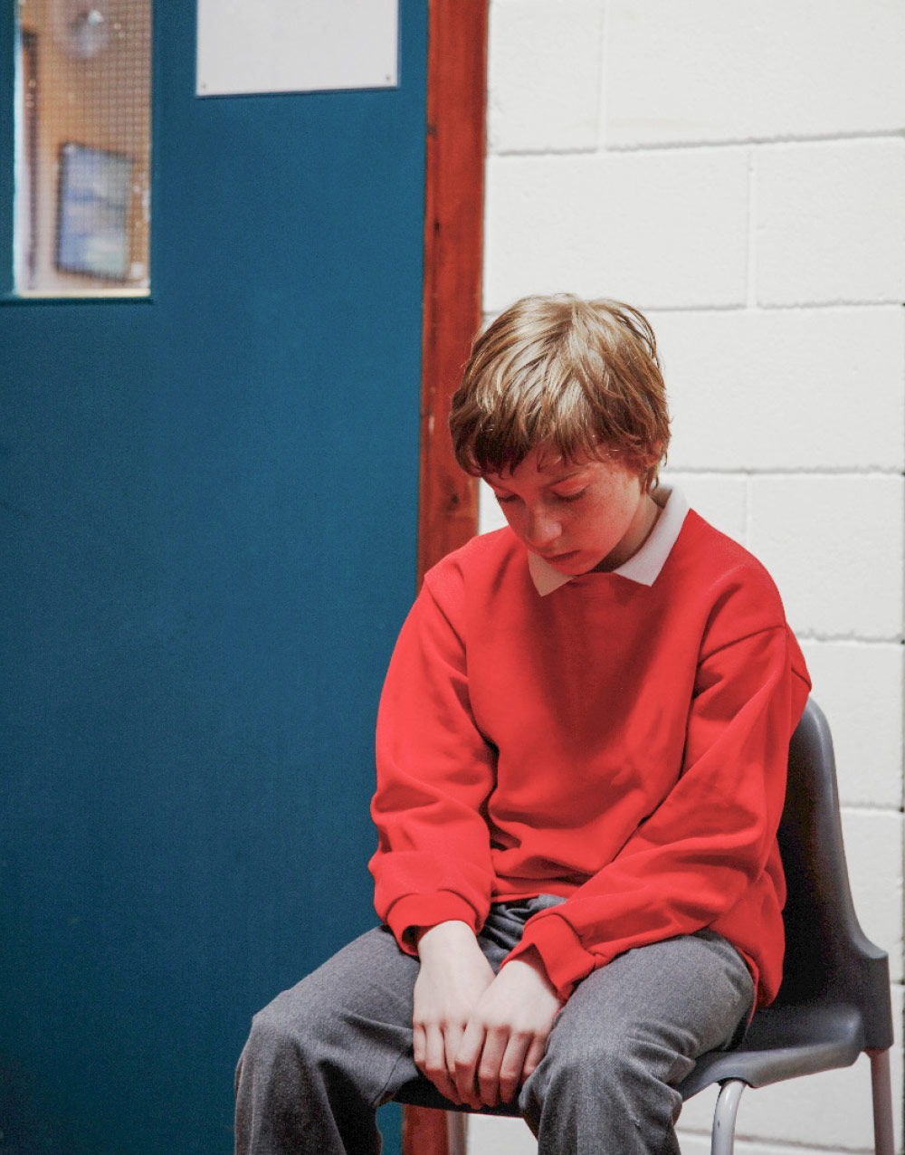 boy sitting on chair outside of classroom door