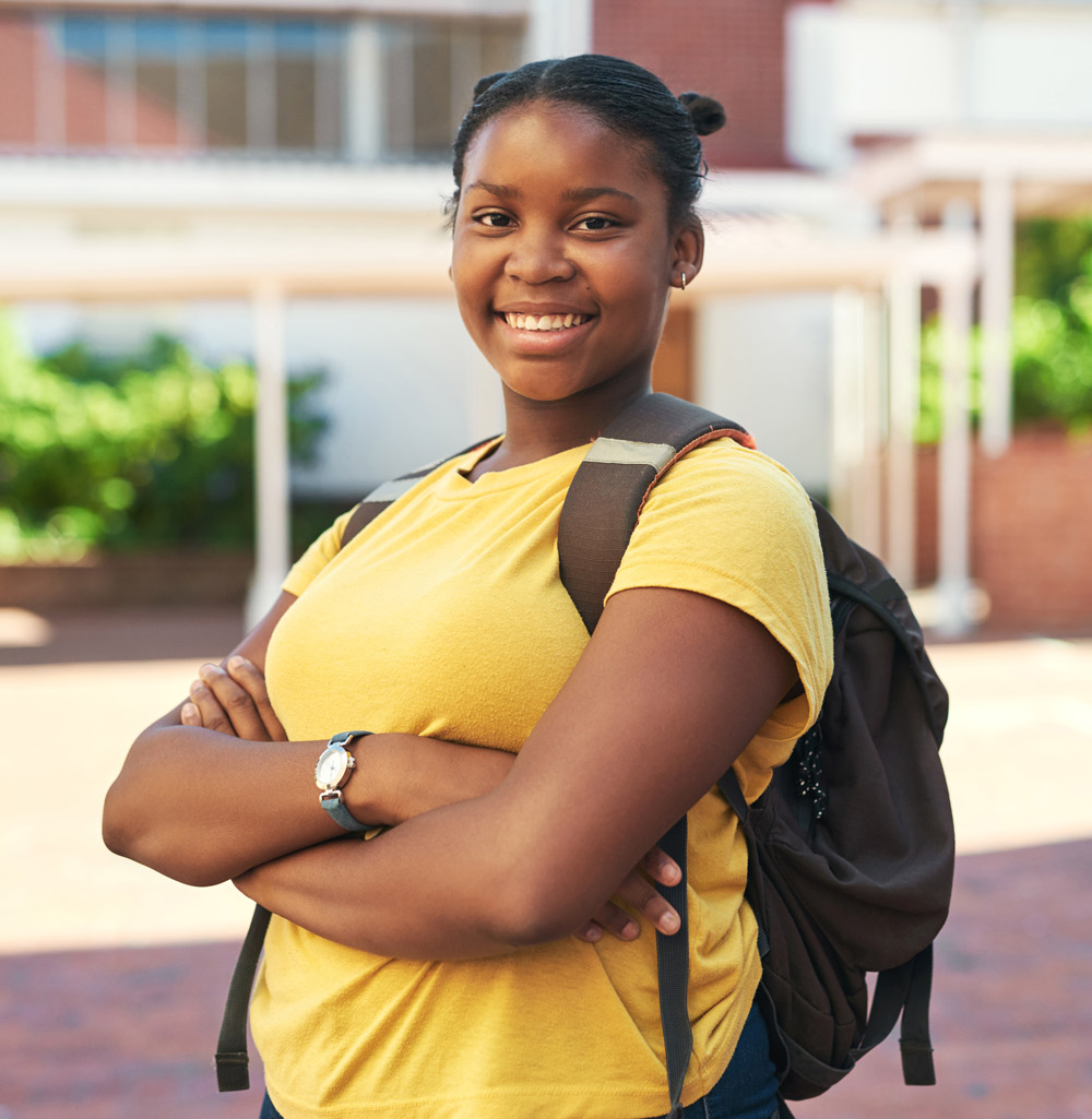 girl smiling with her arms crossed while wearing a backpack and yellow shirt