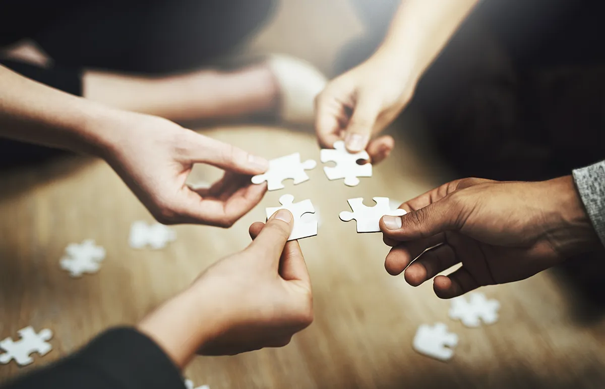 Multiple people holding individual jigsaw puzzle pieces close together