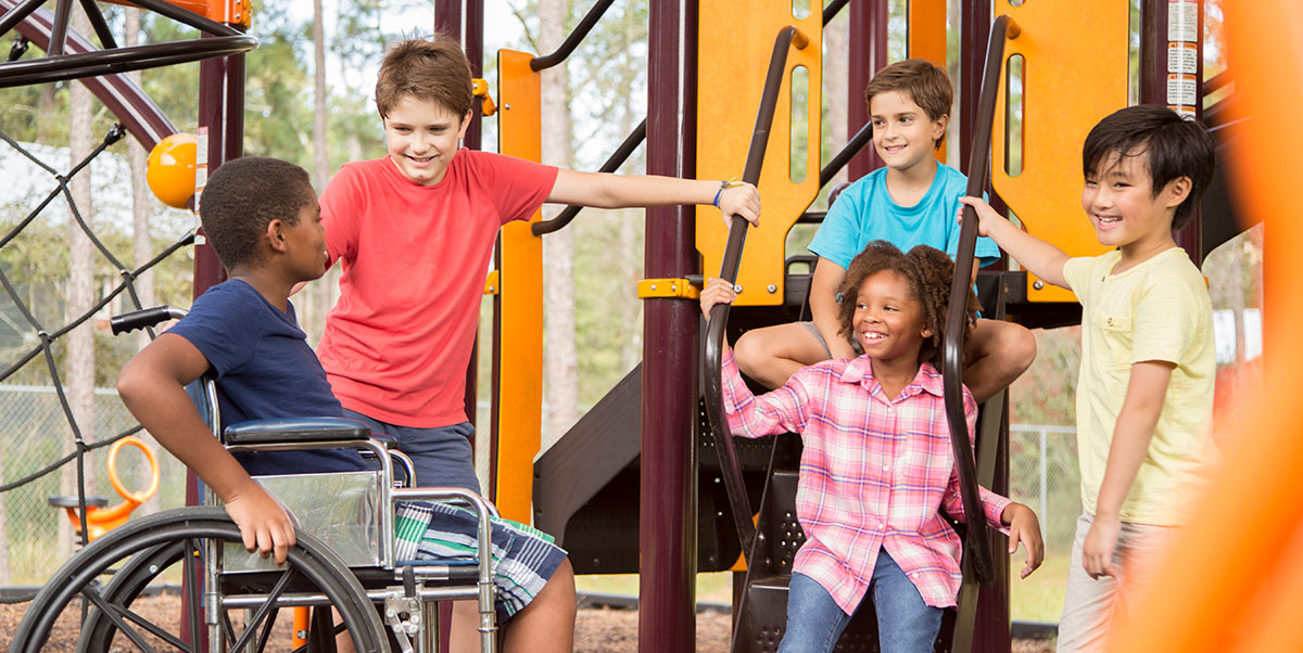 Landscape close-up photograph view of five young kids (four guys and one girl) all smiling and laughing in joy as they all glance at each other at a school playground area outside