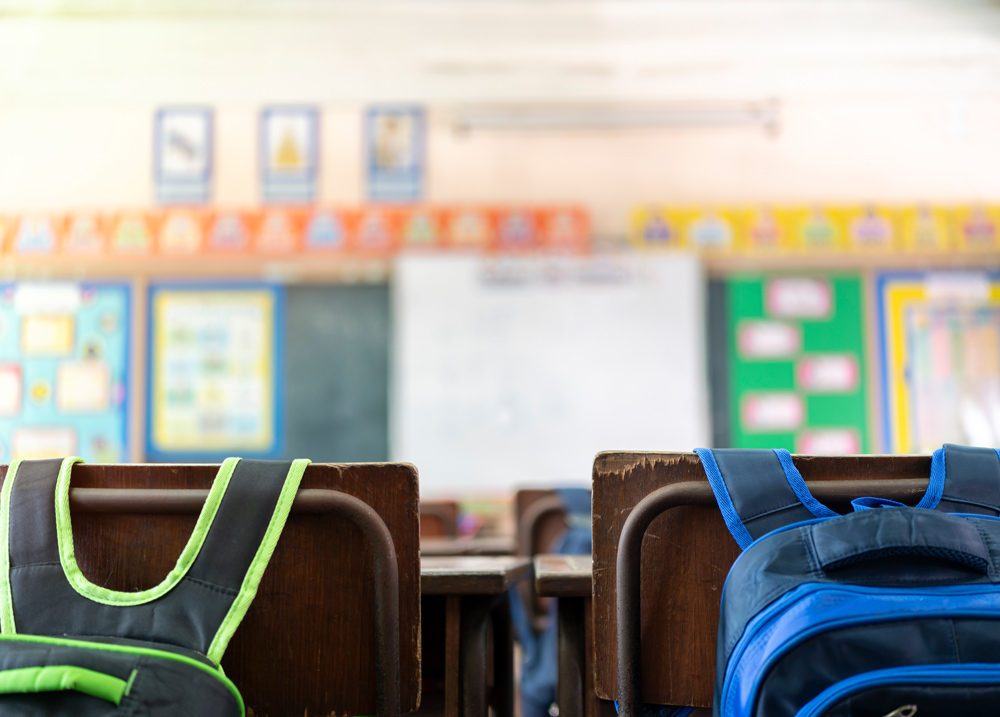 A classroom scene featuring backpacks hanging on the back of chairs