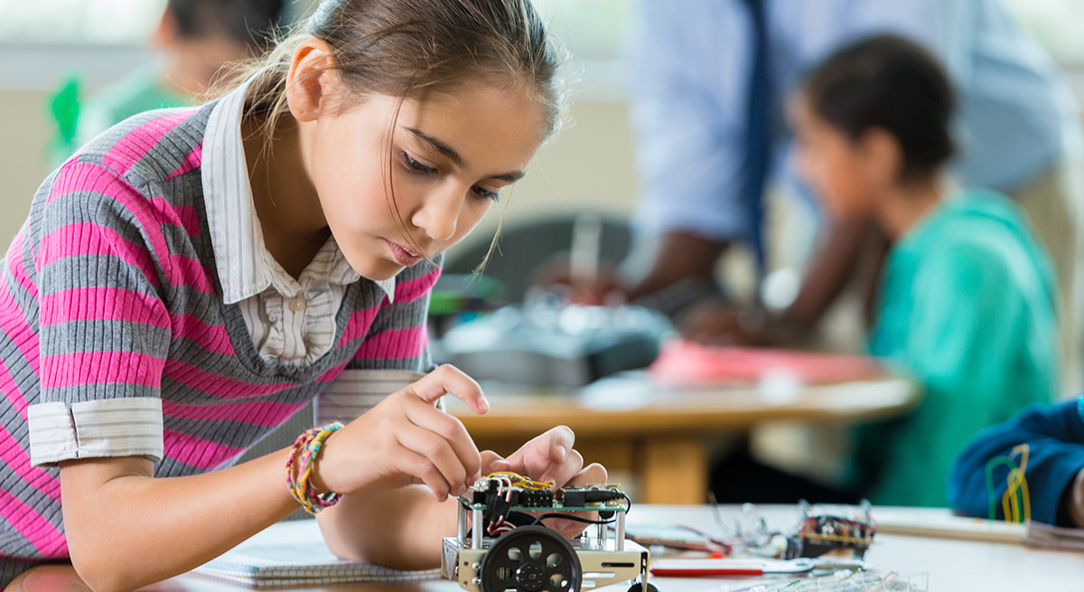 girl fiddling with a robot in a classroom