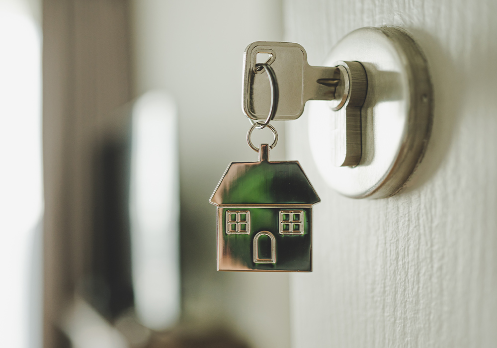 close up of a key, with a house keychain attached, placed in the lock of a door 