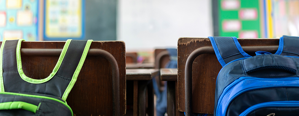 close cropped view of two empty student chairs each with a backpack hanging from the backs