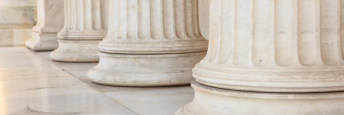 Landscape close-up photograph cropped angle view of four majestic tall elegant marble architectural columns aligned together in a row supporting the facade of a classical historical building, showcasing a striking architectural feature, style, symmetry, and design