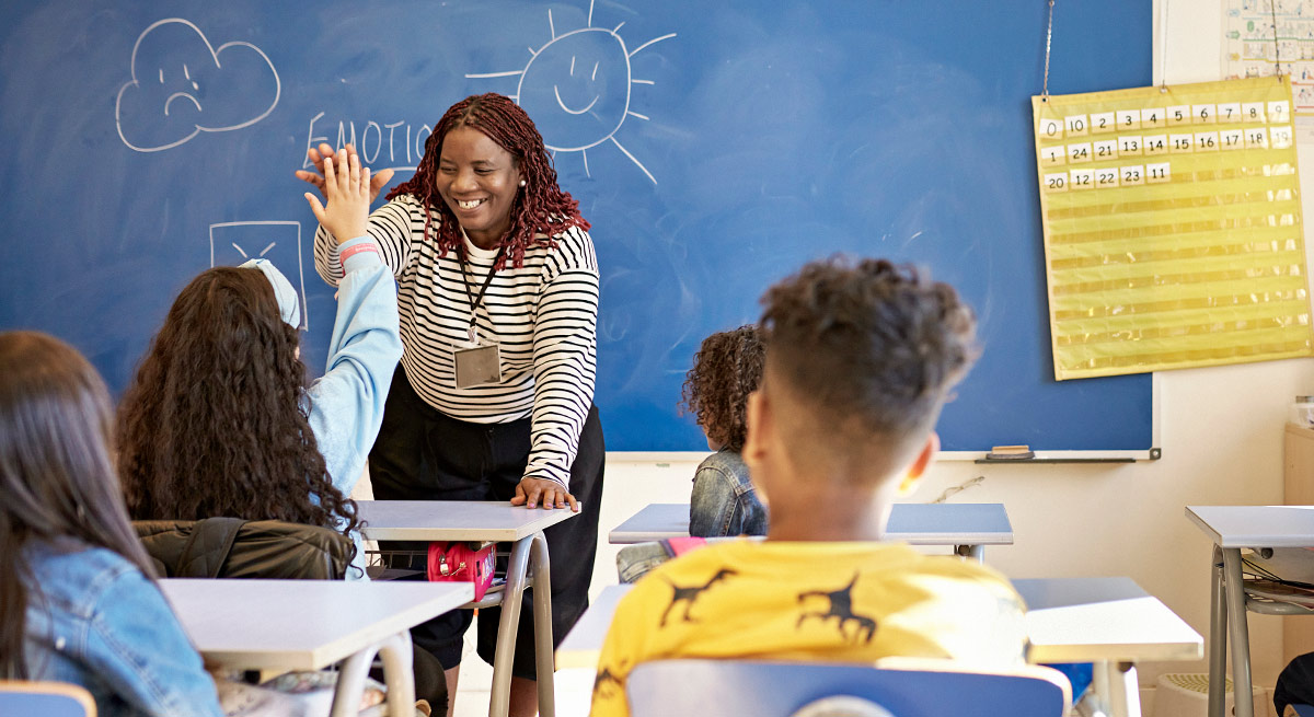 view of kids in a classroom with the teacher giving a high five to a student in the front