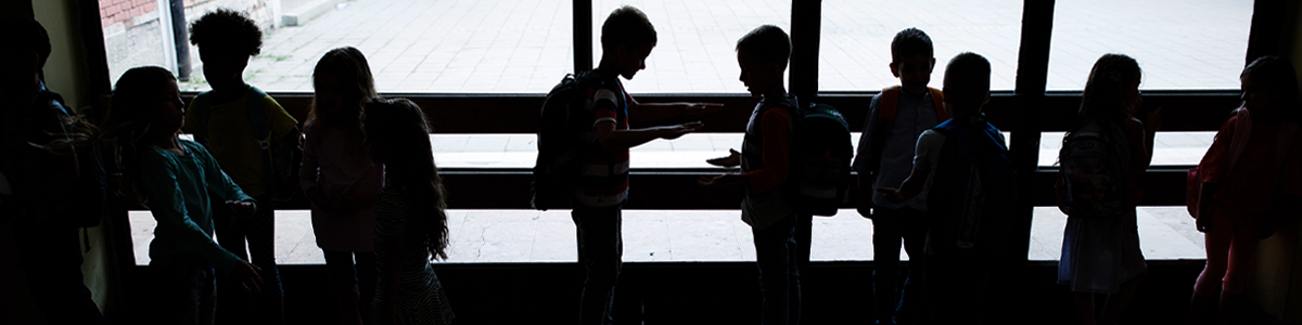low lit image of kindergarten aged children seen only by their silhouettes standing against a wall of windows