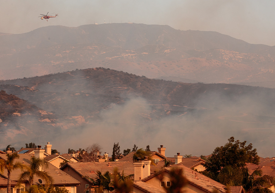 smoke rising during sunset with houses in the forefront and a helicopter flying in the background