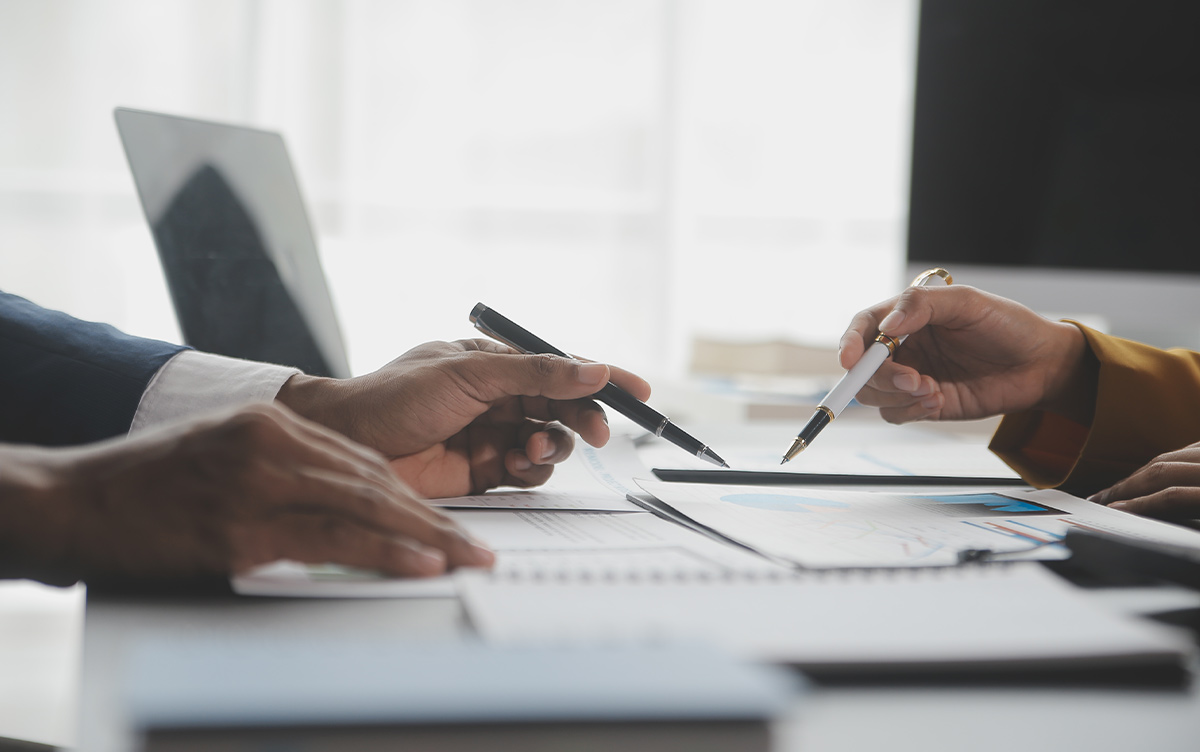 close up of hands holding pens pointing to documents on a desk