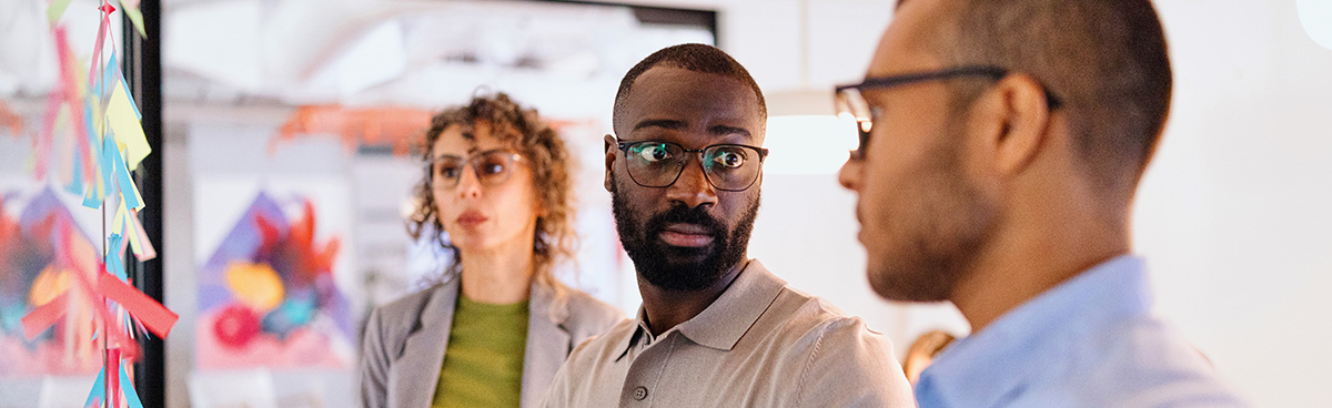 three people wearing business casual attire looking at each other and at sticky notes on a wall