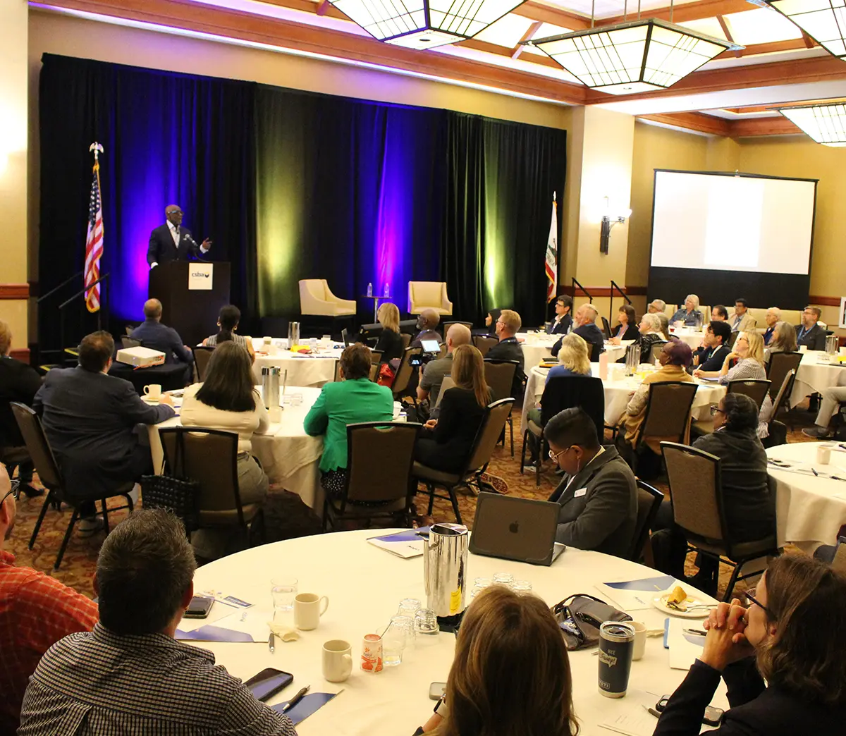 attendees sitting at round tables watching to Chris Gardner's presentation
