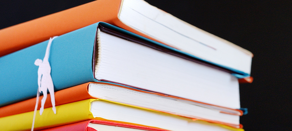 paper cut figures hang from a large stack of colorful book stack
