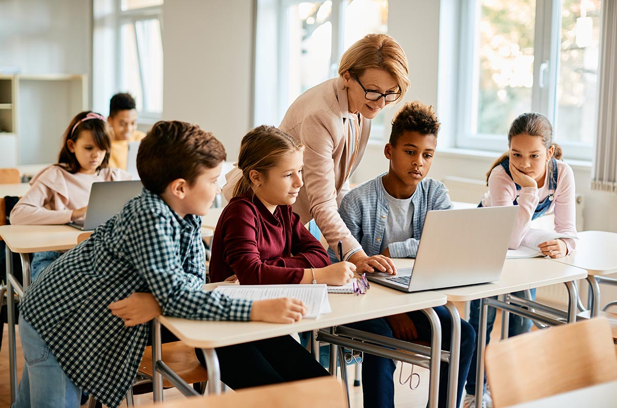 teacher helping students use laptop