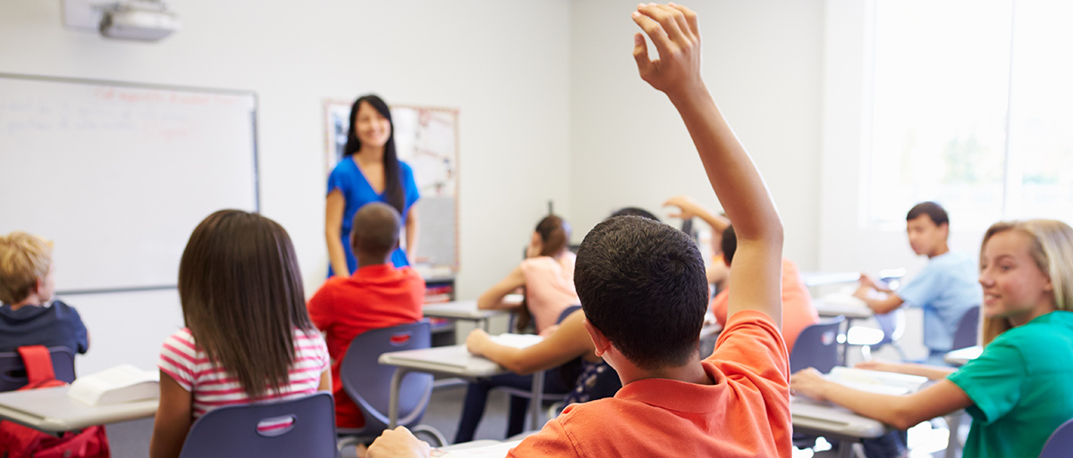 students in a classroom with one student in an orange shirt raising his hand