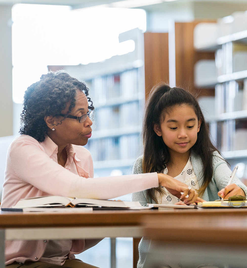 A teacher helps a student with her work in a library.