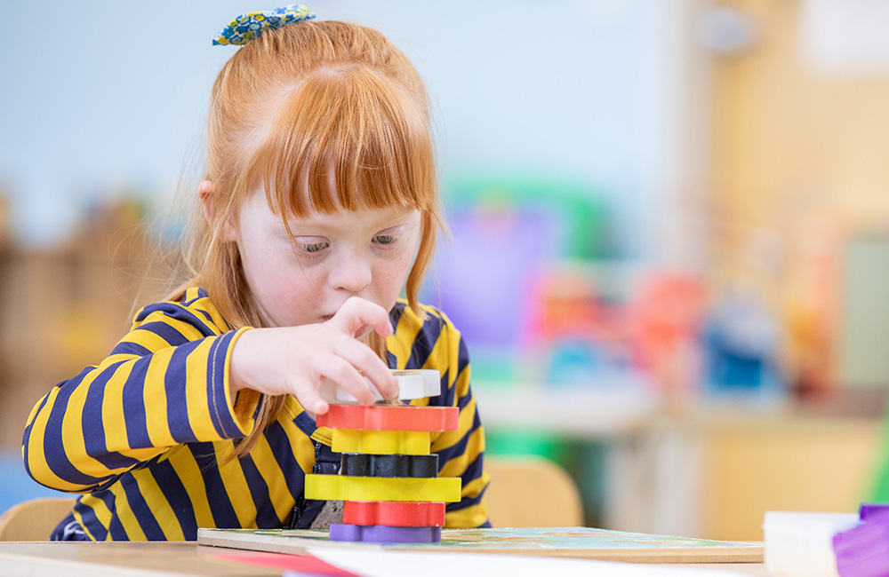 A young girl with red hair plays with colorful blocks.
