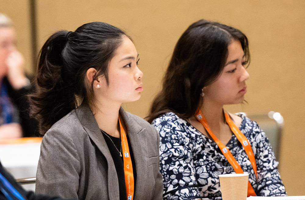 cropped view of two female student board members wearing matching orange lanyards around their neck while attending a meeting in a conference room