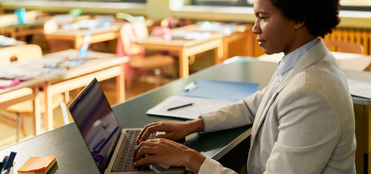 teacher typing on laptop in classroom 
