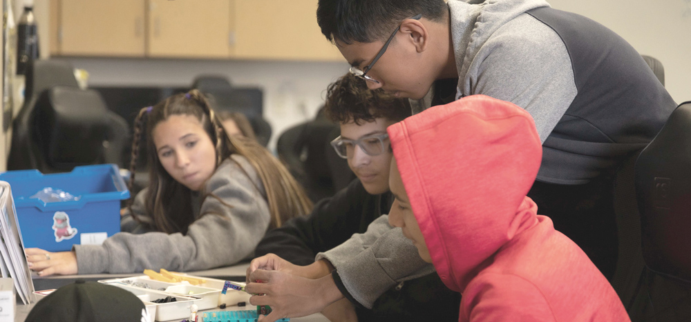 Photo of four high school students collaborating on a project at a classroom table.