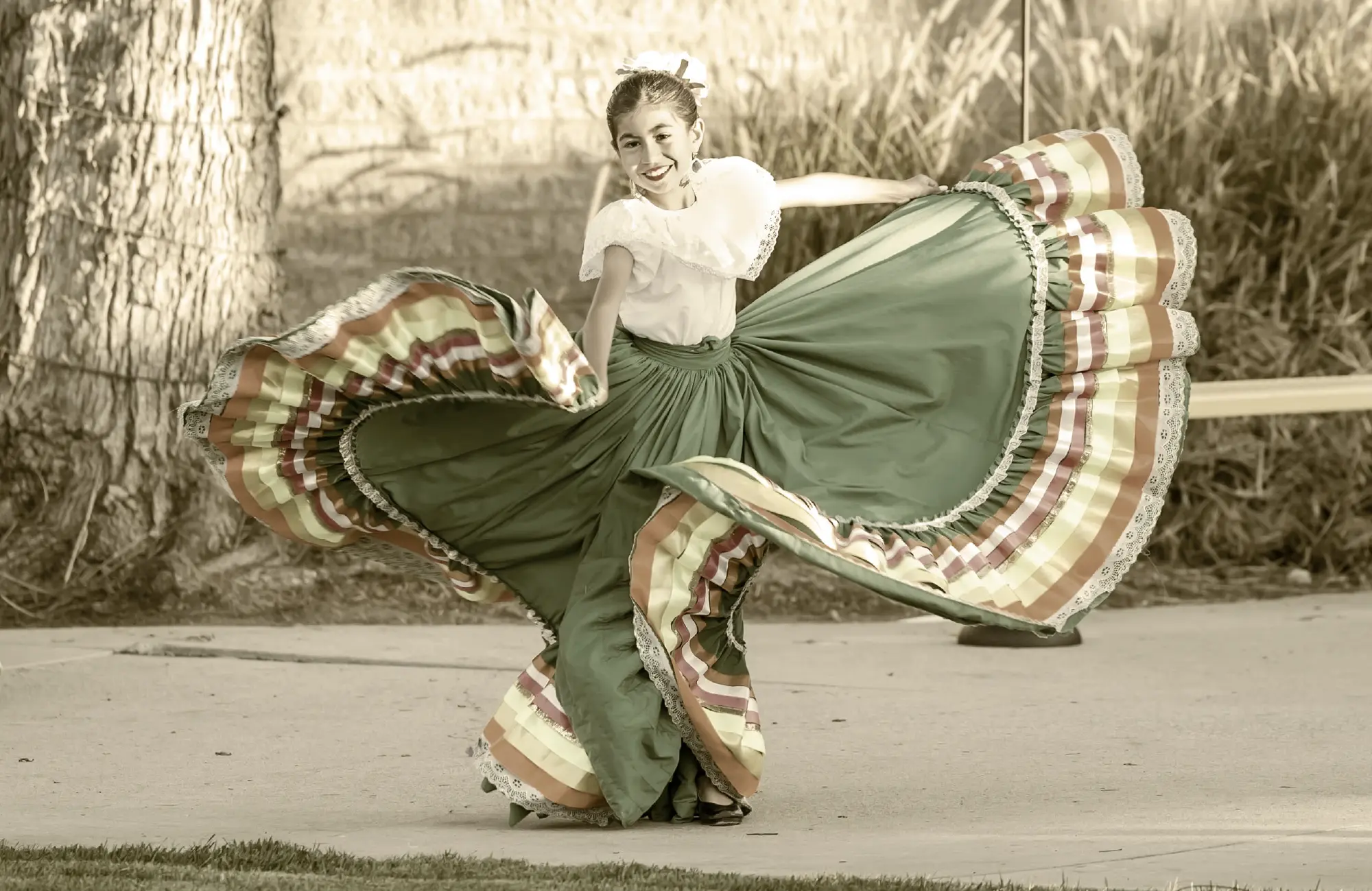 a young girl performing a folkloric dance, smiling while swirling her elaborate green and striped skirt outdoors