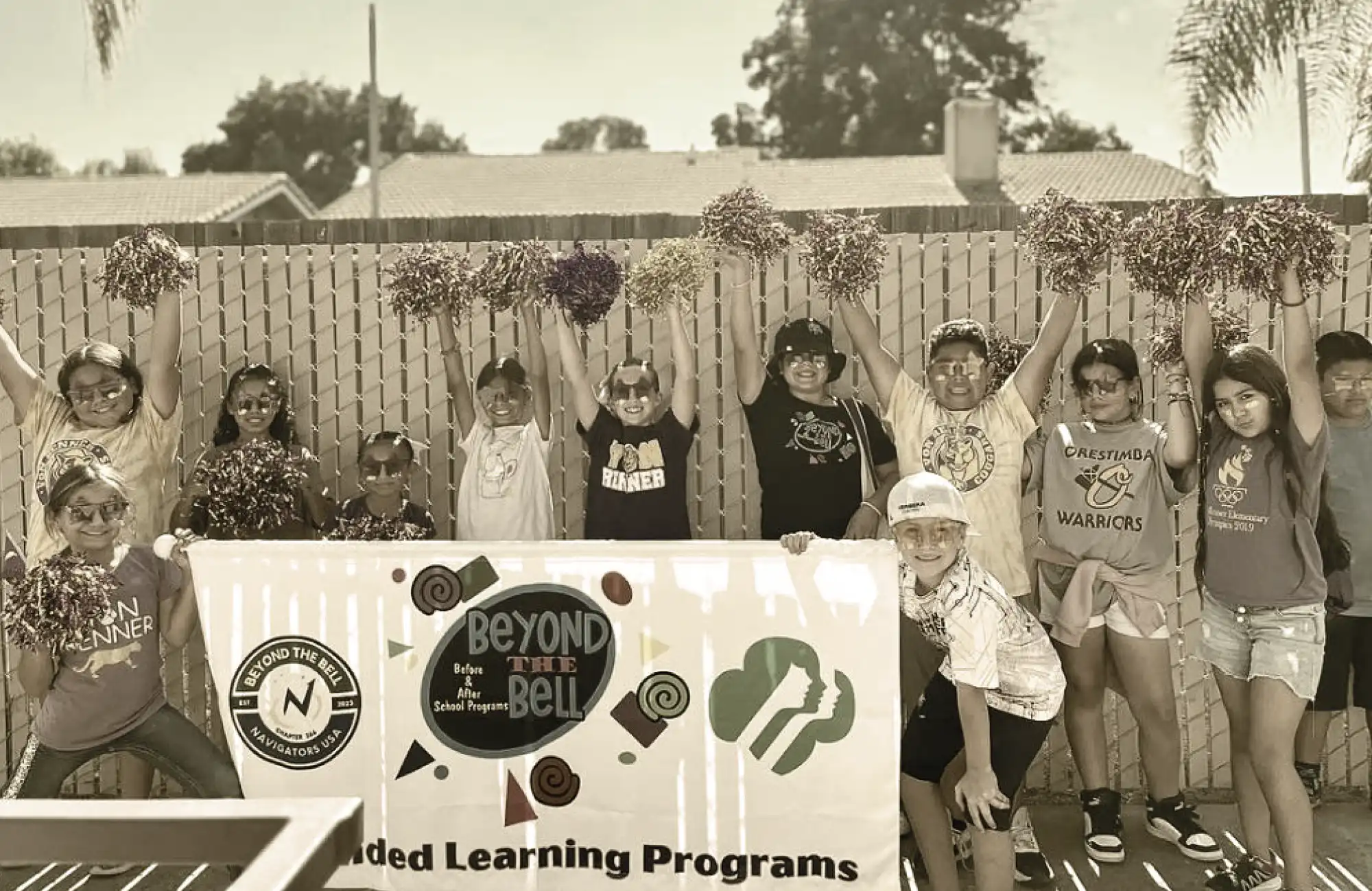 A group of smiling students holding pom-poms behind a banner for the "Beyond the Bell" after-school program.