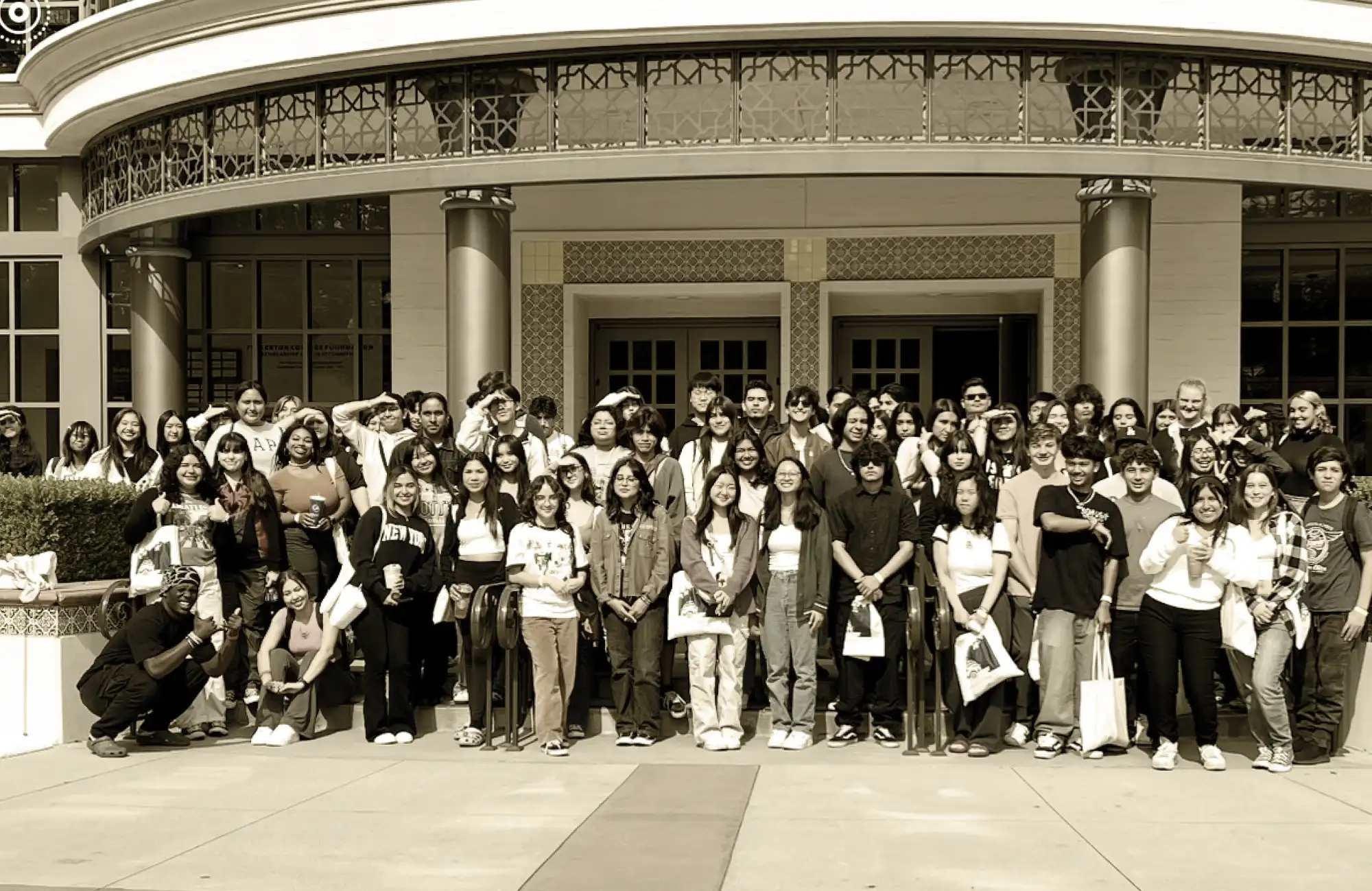 A large group of high school students smiling and posing in front of a grand, curved building entrance.