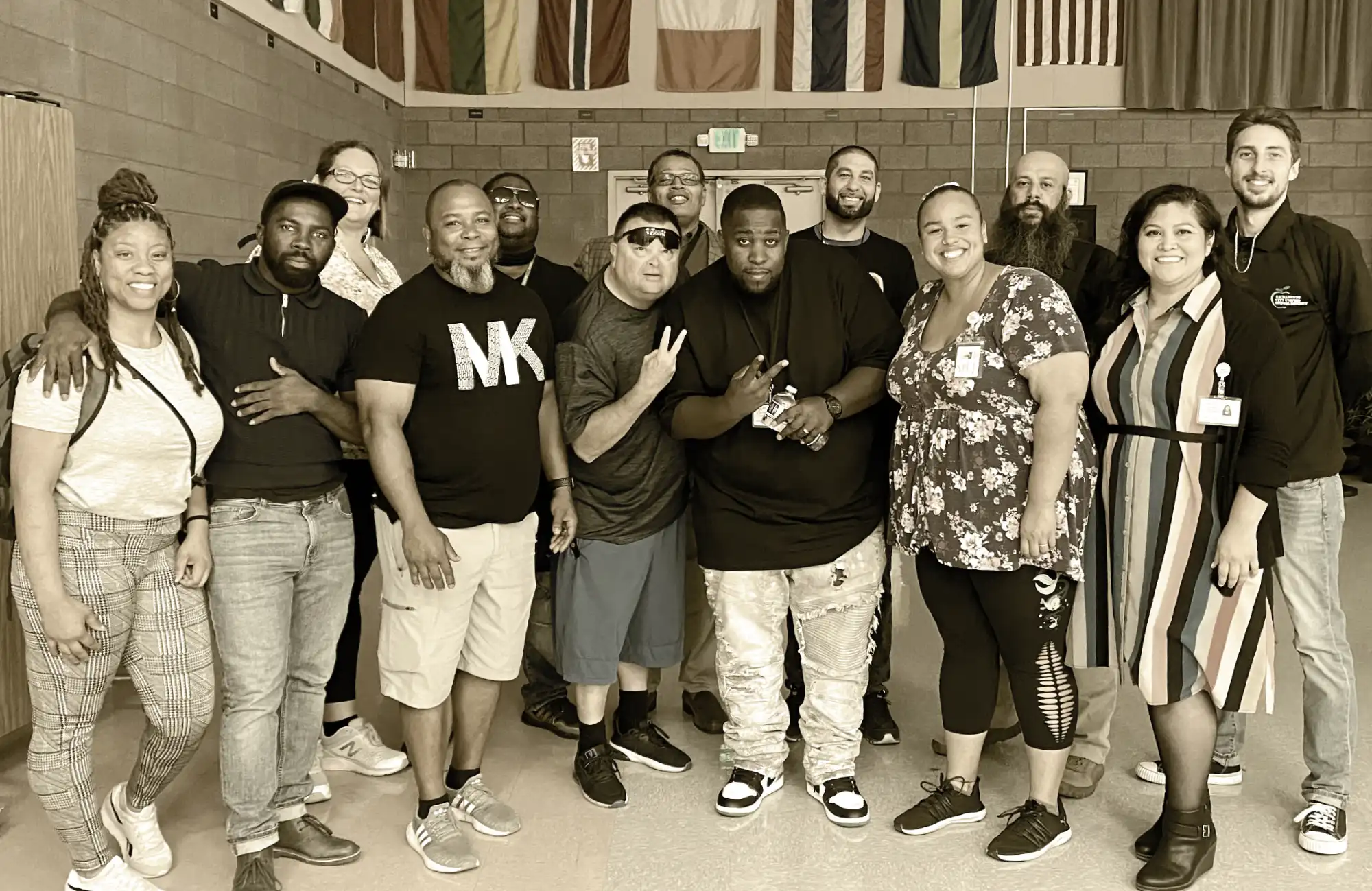 A group photo of 13 adults in a school setting, smiling for the camera in front of a display of international flags.