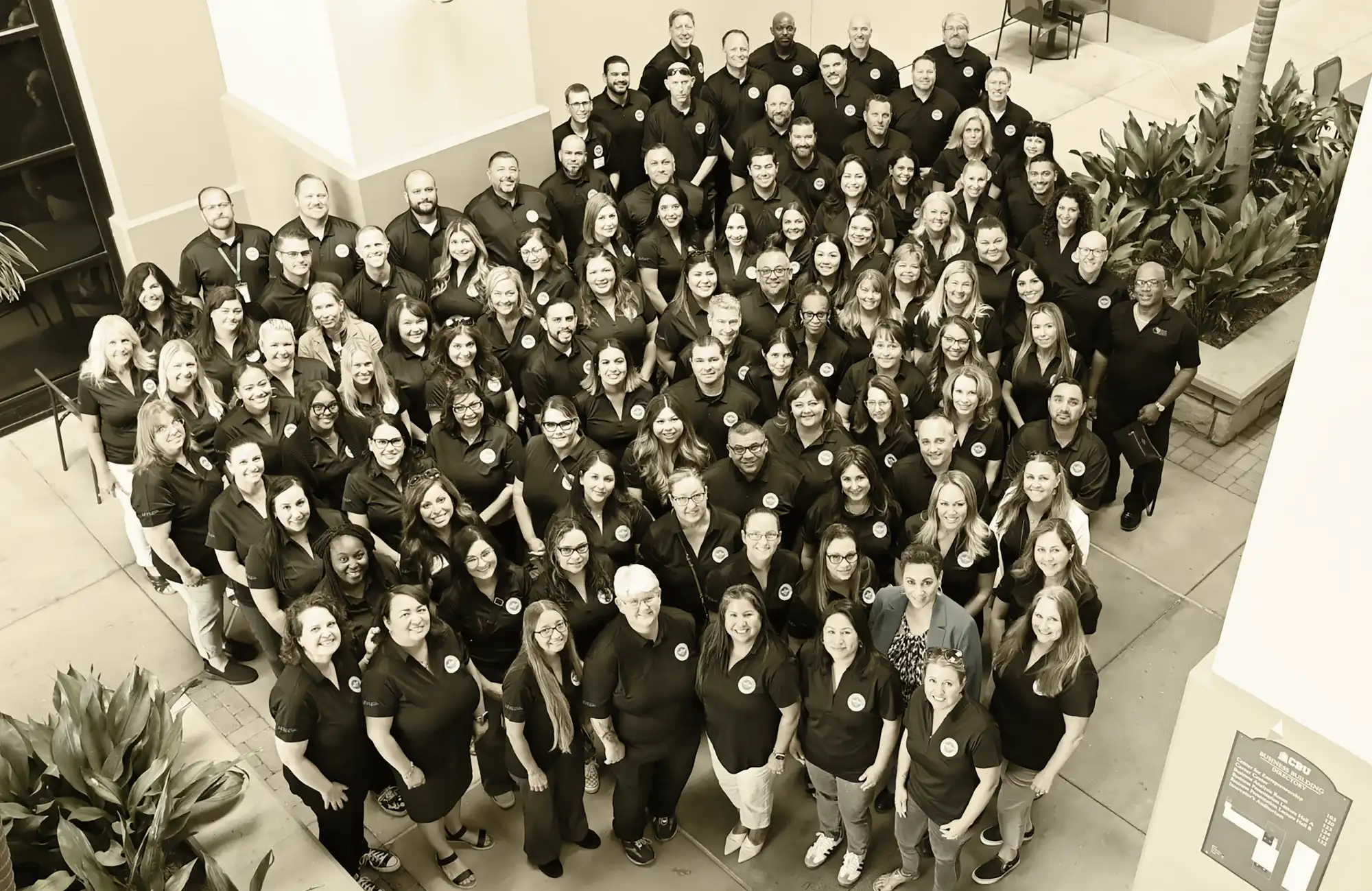 A large group of adults wearing matching dark shirts and smiling for a professional learning event.