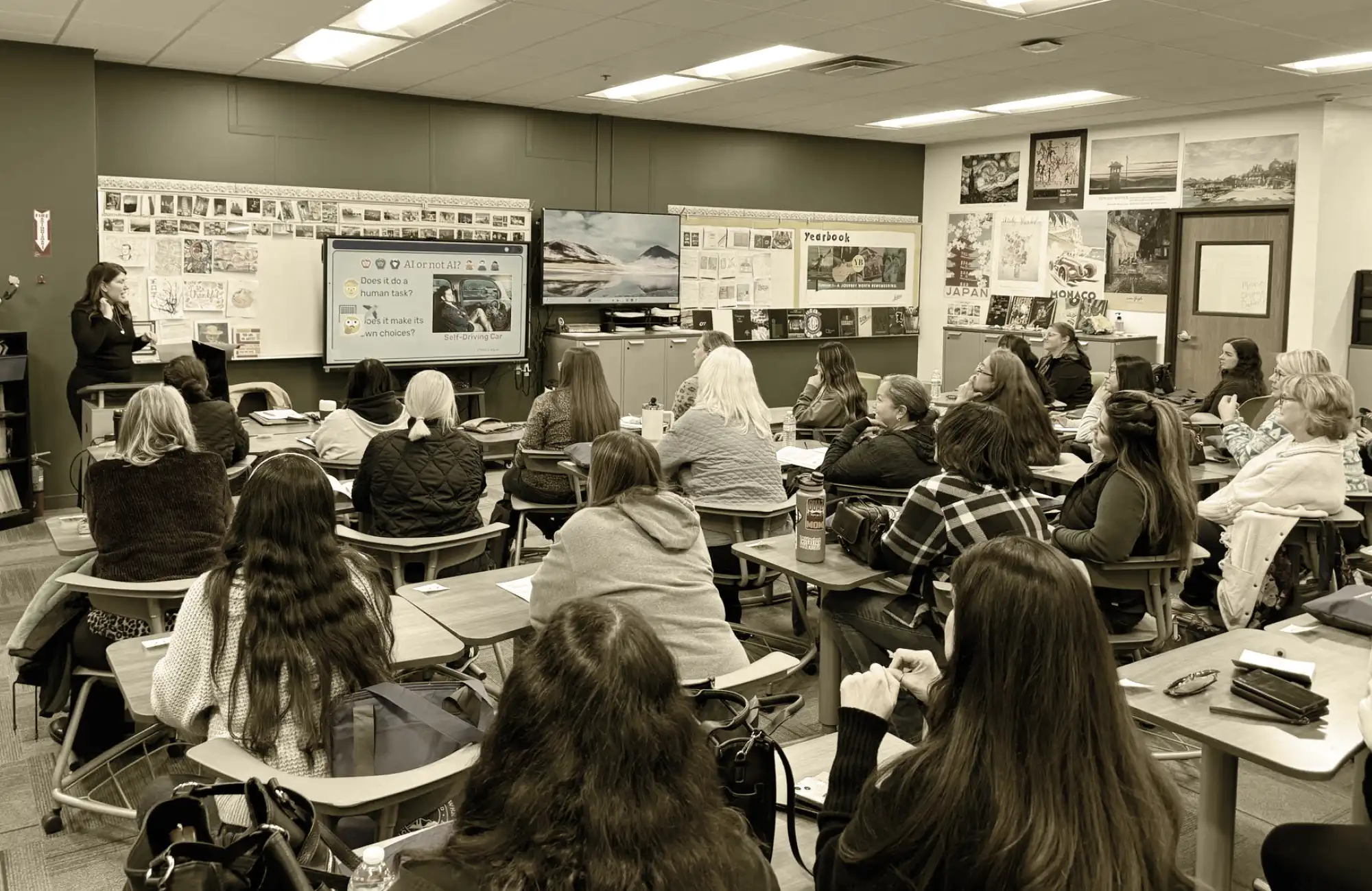 A female instructor presenting in a classroom to a large group of adults seated at desks.
