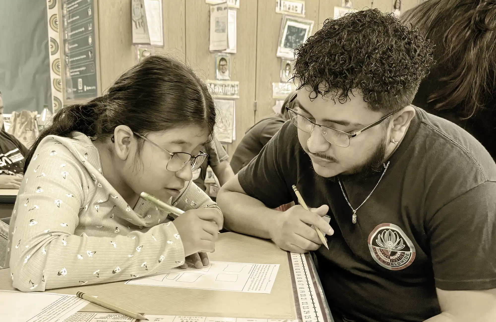 High school mentor working closely with a young female student on a worksheet at a classroom desk.