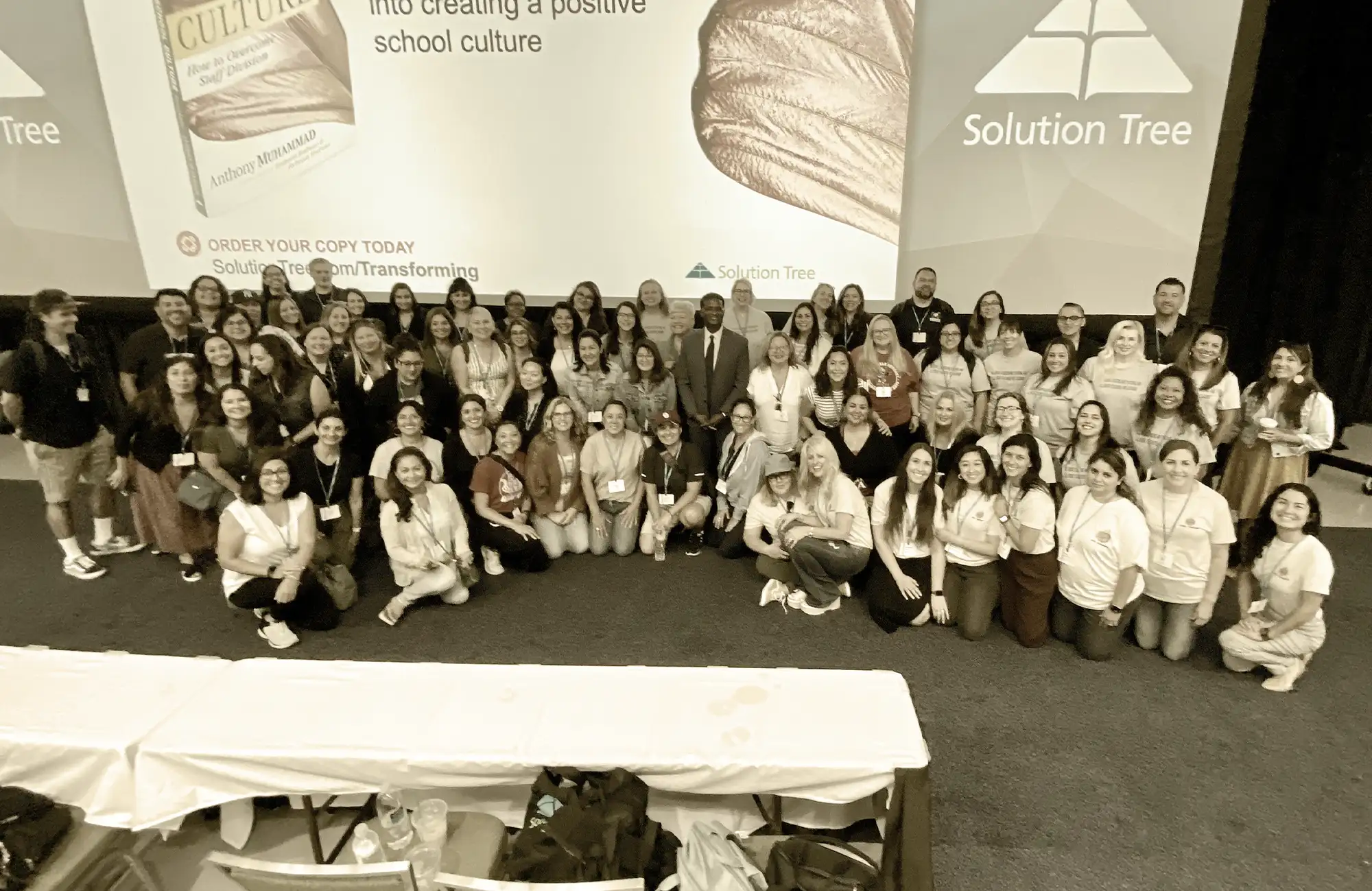 Large group of educators and professionals posing for a group photo at a Solution Tree conference in front of a banner promoting a book on school culture.