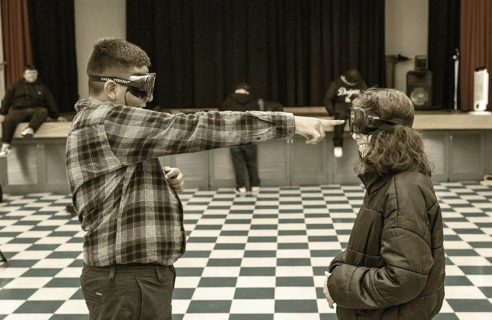 Two students wearing virtual reality or simulation goggles, engaging in a CTE scenario on a black and white checkered floor.