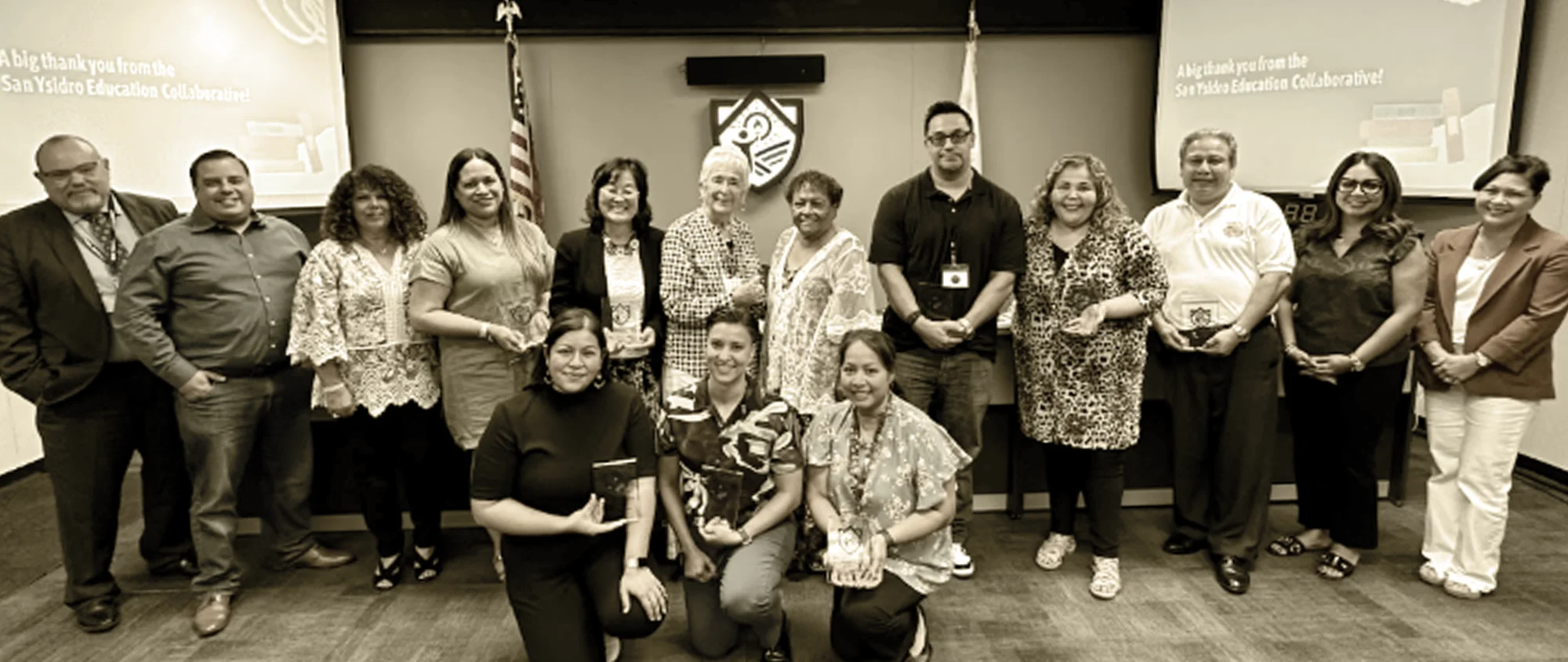 Group of educators and community partners from the San Ysidro Education Collaborative posing with awards in a government or school board room.