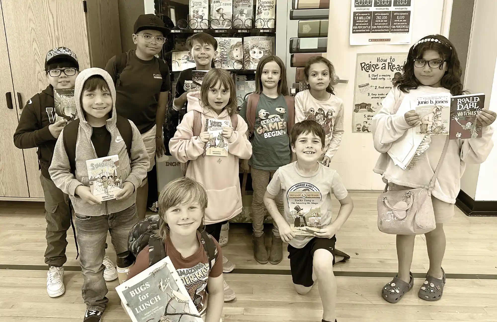 Group of smiling elementary school children holding various books they selected from a book vending machine in the school.