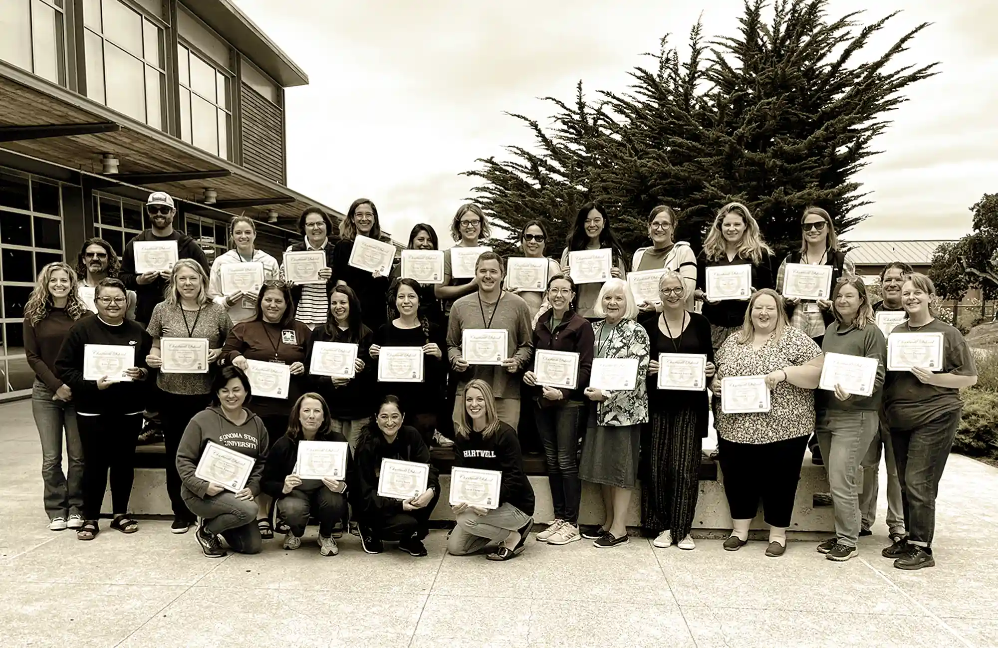 Large group of educators posing outdoors, holding up certificates after completing a professional development or curriculum training program.