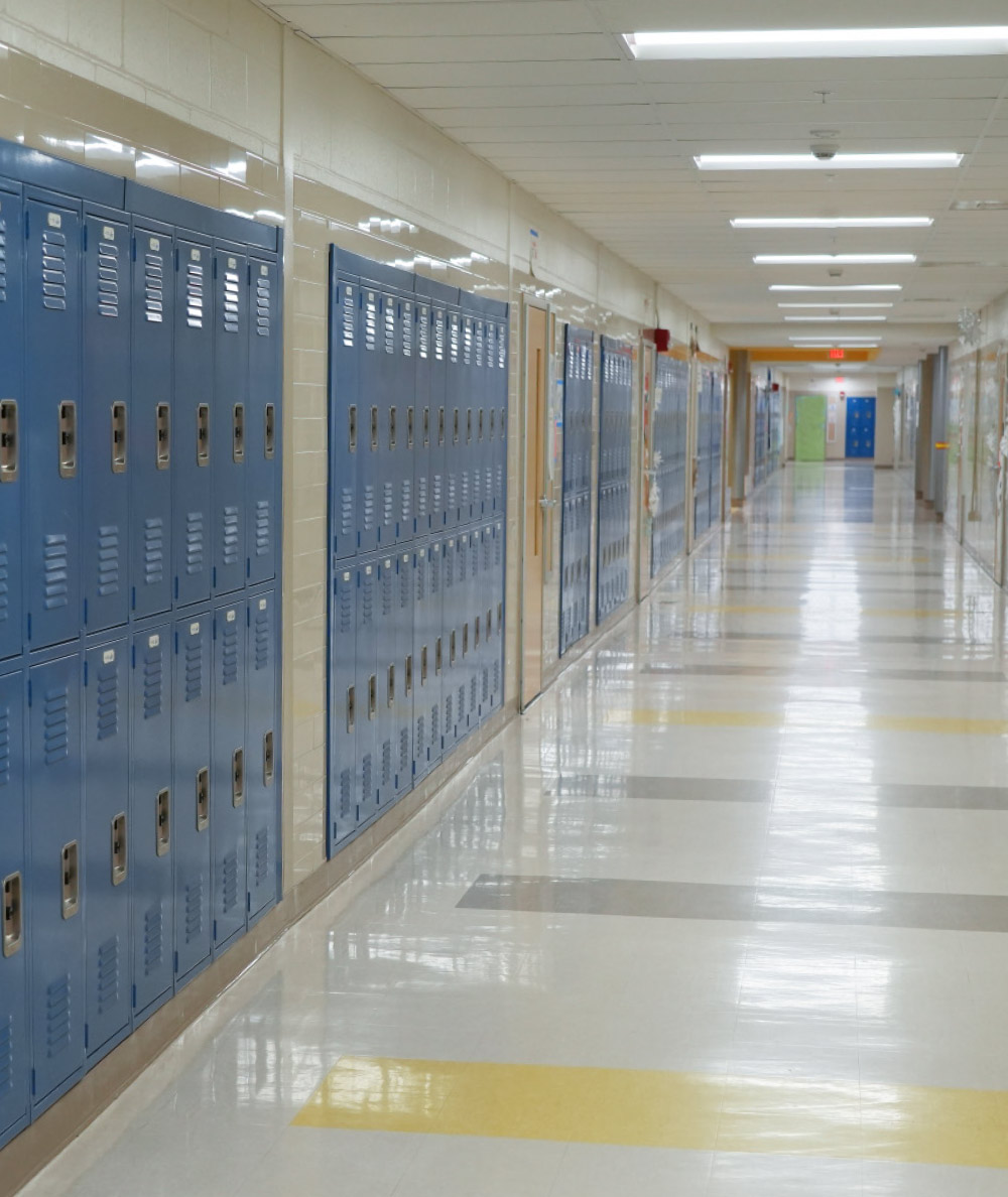 A long, brightly lit school hallway with rows of blue metal lockers on the left and a reflective, tiled floor.
