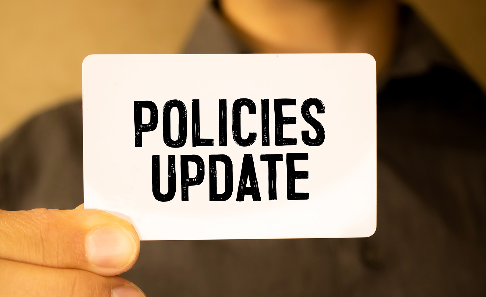 Close up of a persons hand holding a card that reads “Policies Update”