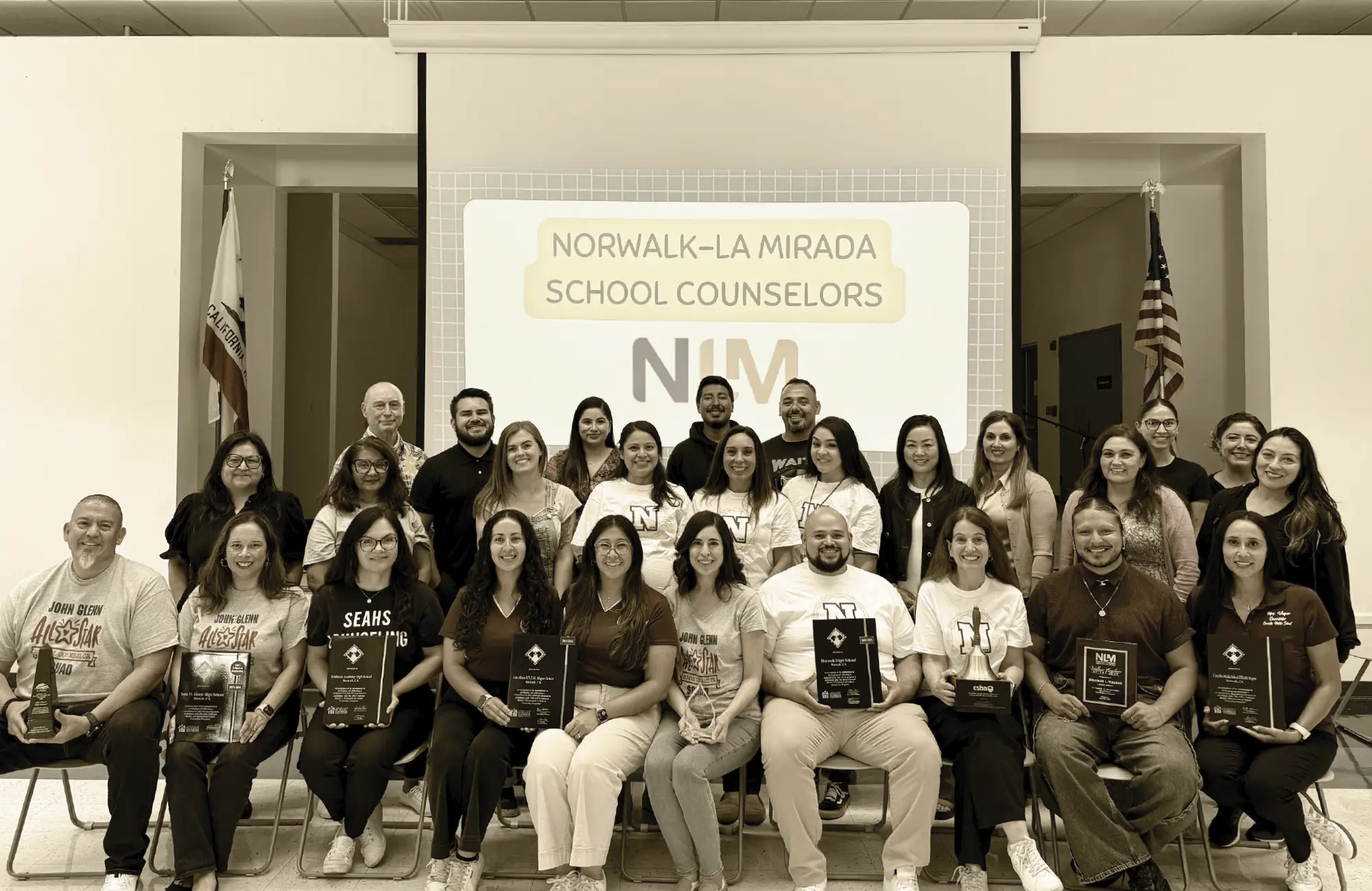 Group photo of Norwalk-La Mirada school counselors and staff holding awards. They are seated in front of a screen displaying "Norwalk-La Mirada School Counselors" and the district logo.