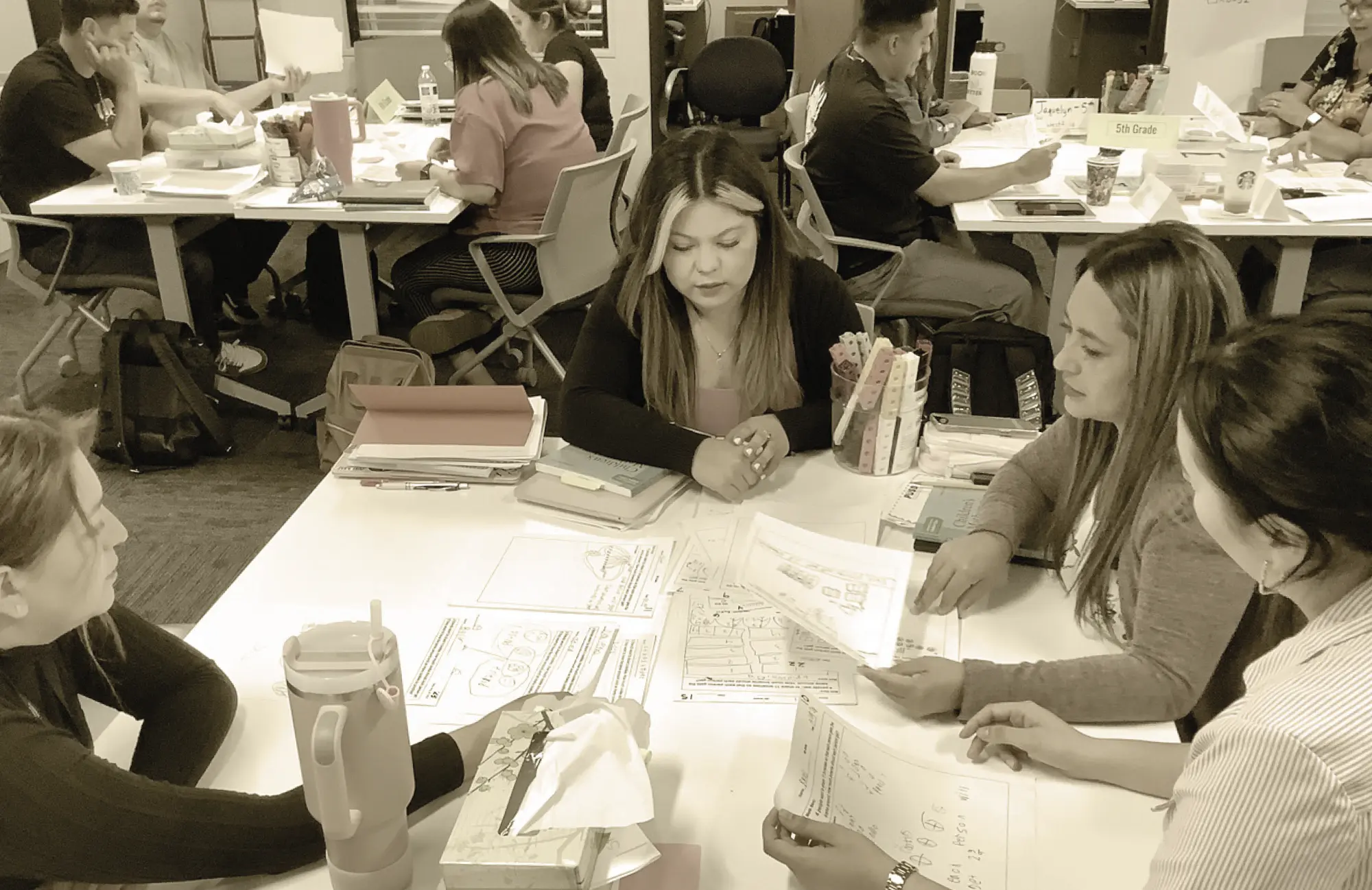 Four educators seated around a white table examining documents and data maps, representing a professional learning community focused on continuous, data-driven improvement.