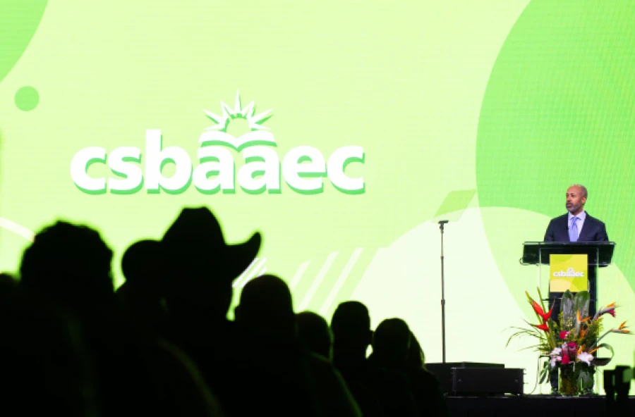 Professional speaker at an educational leadership summit, silhouetted audience members watching a presentation on a bright green stage with the CSBA AEC logo