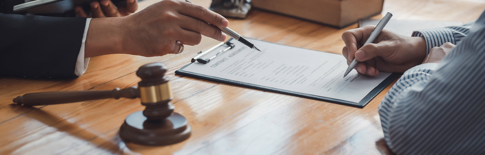 Close-up of two people in a law office reviewing and signing a legal document on a clipboard.