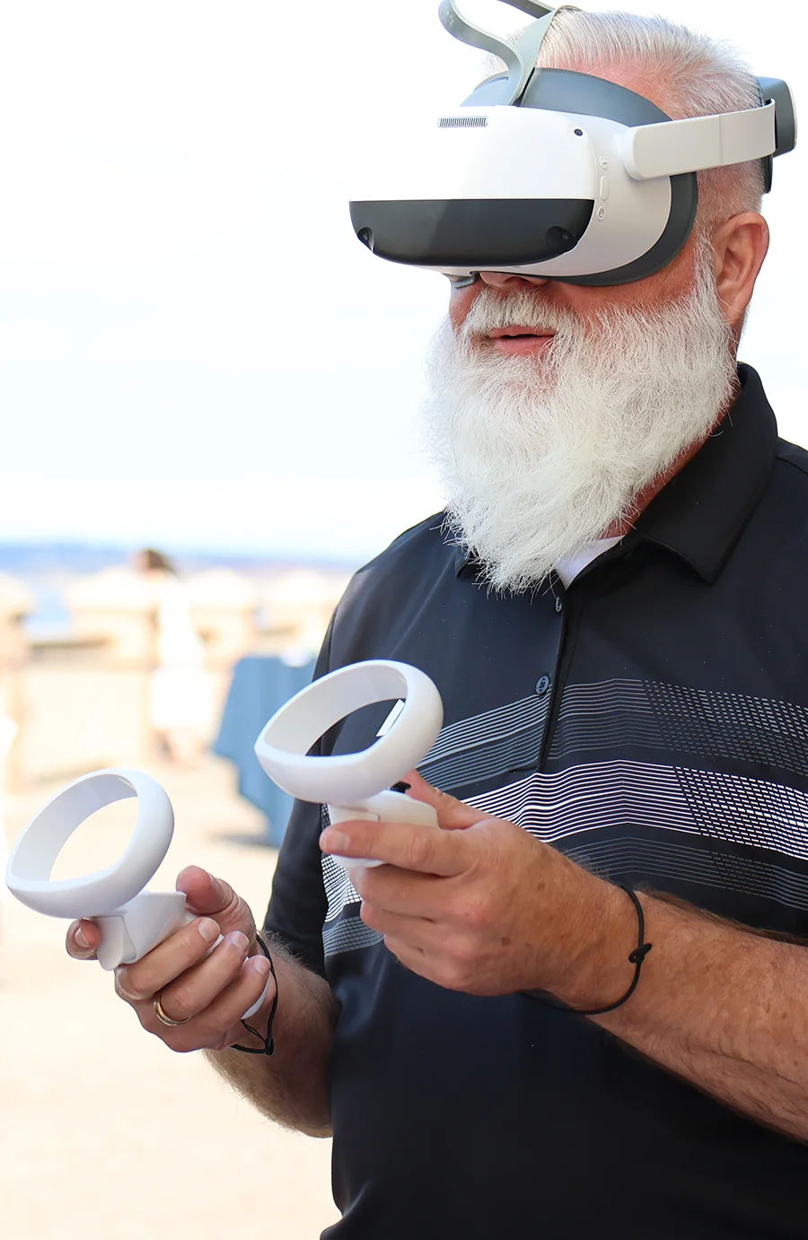 A professional with a white beard using a VR headset and handheld controllers during a member services technology demonstration.
