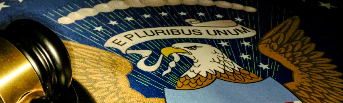 Close-up of a legal gavel resting next to the Great Seal of the United States featuring the eagle and "E Pluribus Unum" banner.